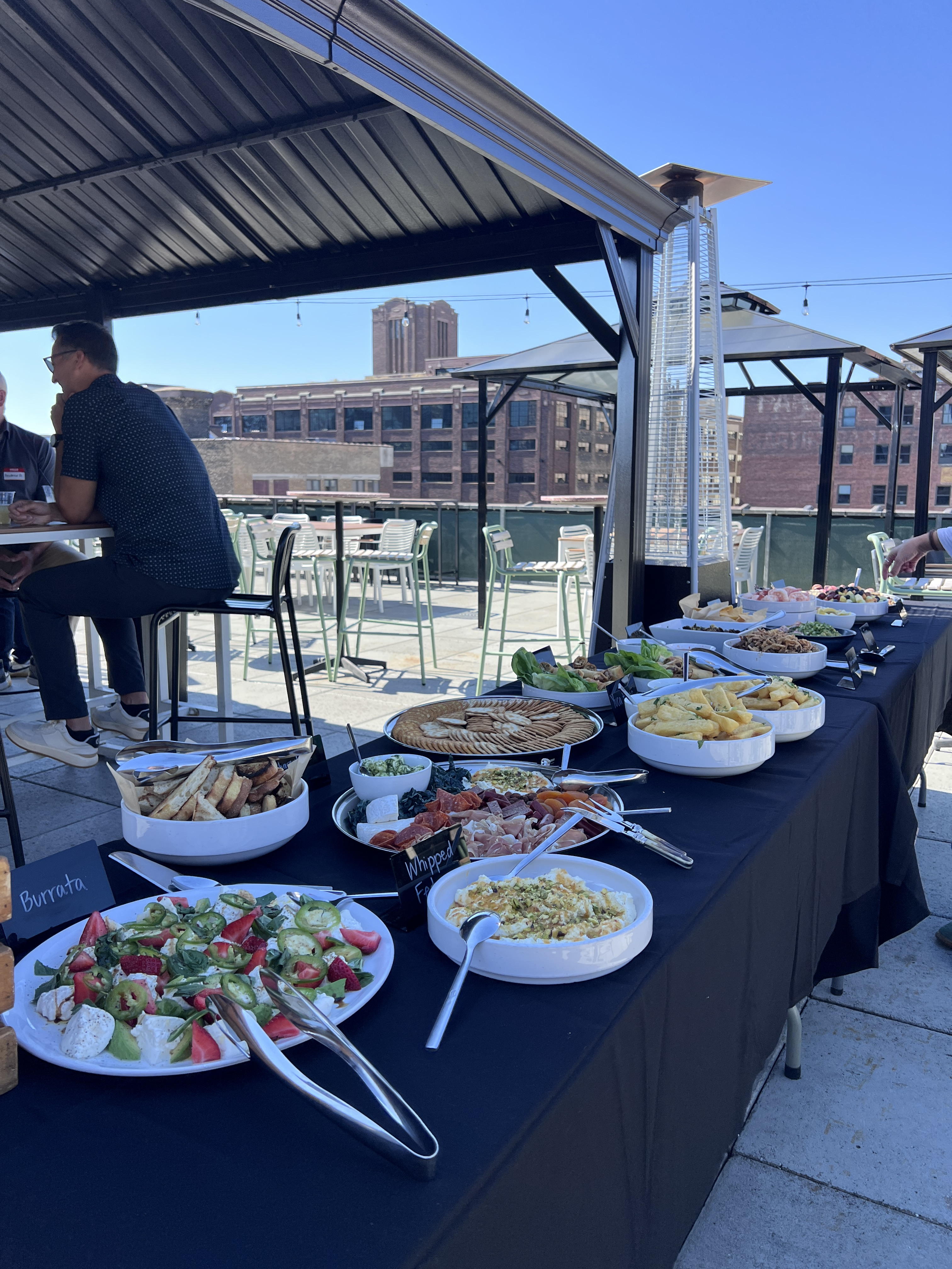 Rooftop spread at NOLO's with burrata, whipped feta, charcuterie, and yuca fries as guests talk under a canopy