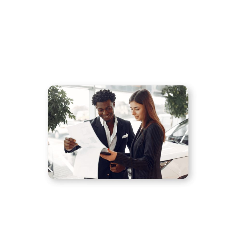 two people reviewing a contract with a car in the background