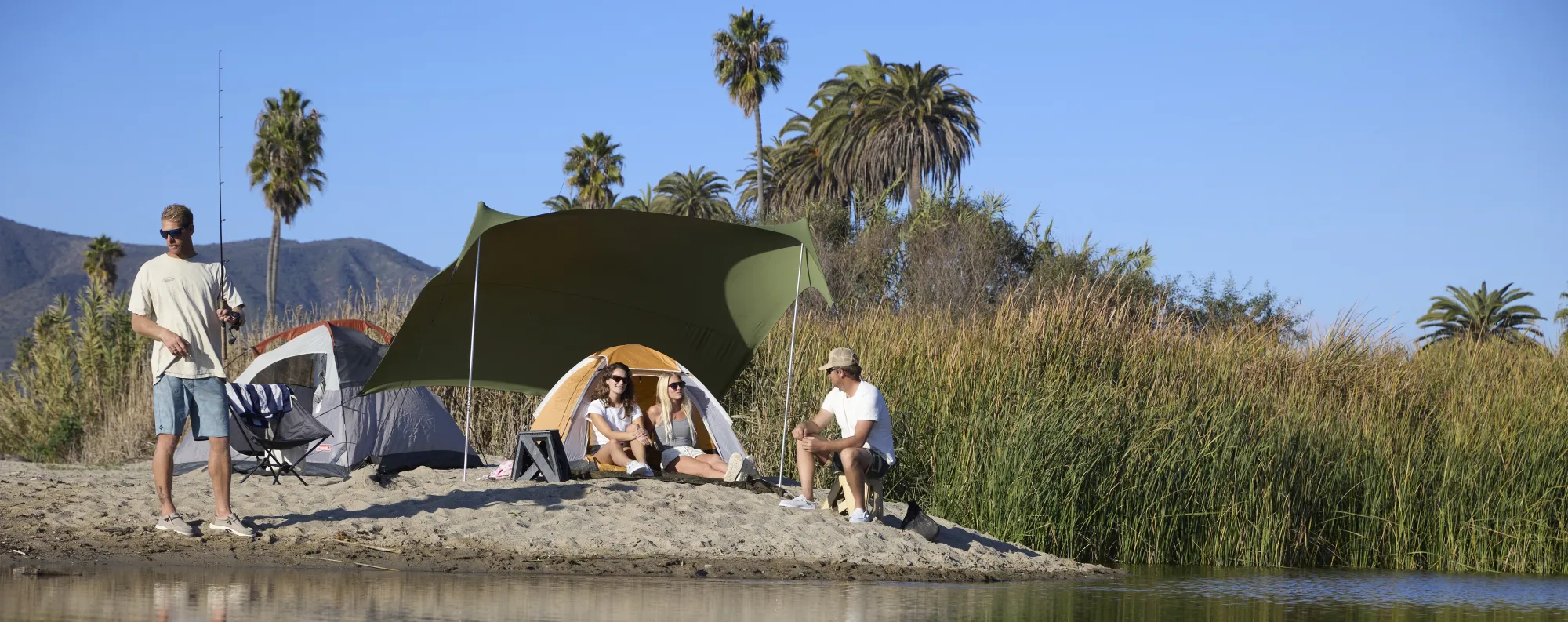 A group of friends camping near the side of a lake.