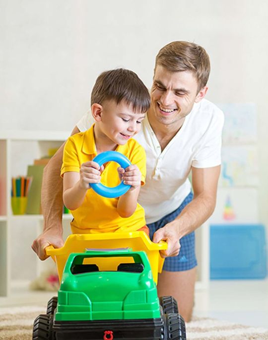 father playing with son riding on a toy truck