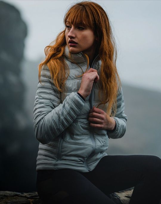 A woman sitting on a rock zipping up her jacket.