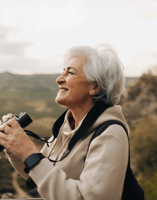 An older woman looking into the sky while holding a pair of binoculars.