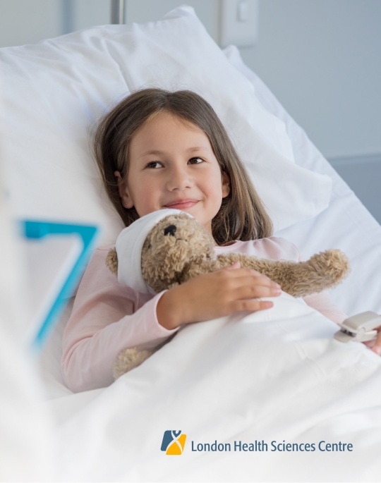 Child smiling in a hospital bed with a teddy bear