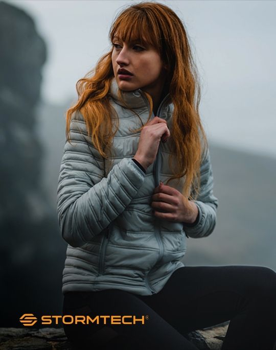 a woman sitting in a rock zipping up her jacket